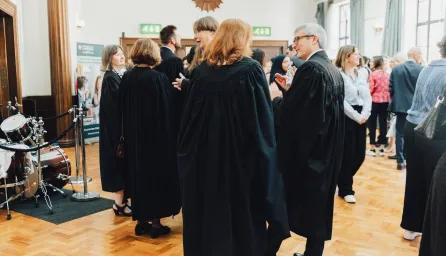 A large reception room full of Cambridge academics in black gowns and other people chatting and mingling. 