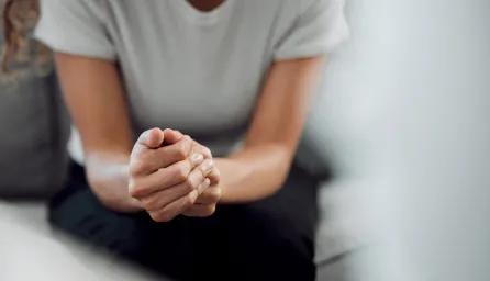 A person with clasped hands leaning forward on a couch