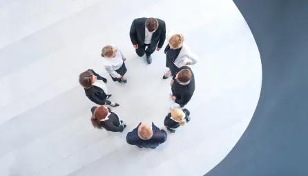 Group of 8 people pictured from above, dressed in business clothing and standing in a circle. 