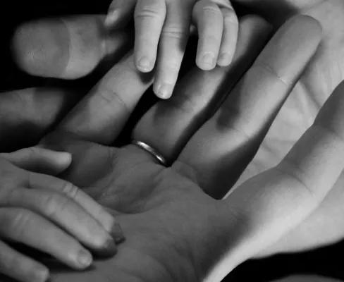 Black and white photo of 2 adult palm of hands holding baby hands. 