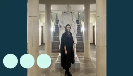 Woman in graduation gown stood in front of a statue 