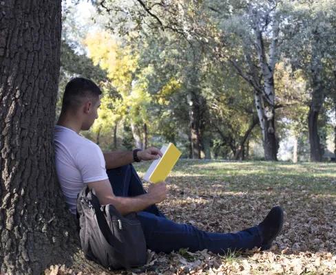 Man leaning against a tree reading a book