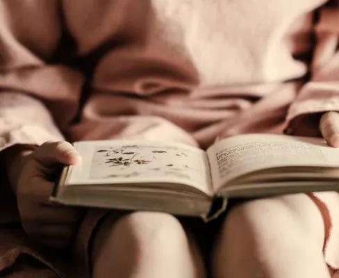 A child sitting on a bed reading a book. 
