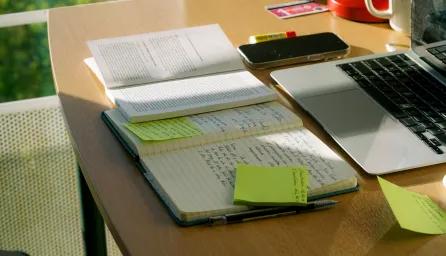 A student's desk with laptop, note book, text book and phone