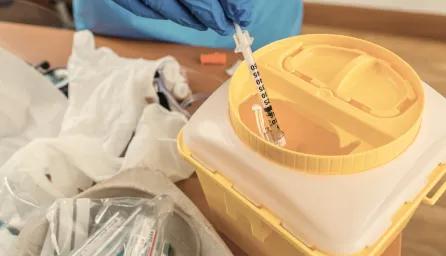 Scientist adding syringe to yellow hazardous waste bin