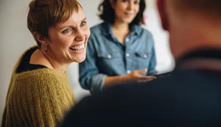 hree people in conversation, with two facing and smiling at the third whose back is to the camera