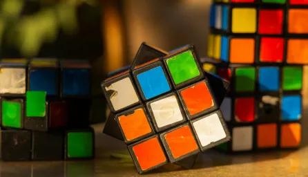 A table with 4 worn and unevenly turned Rubik’s Cubes, showing faded and peeling stickers, with mismatched colours and tilted angles