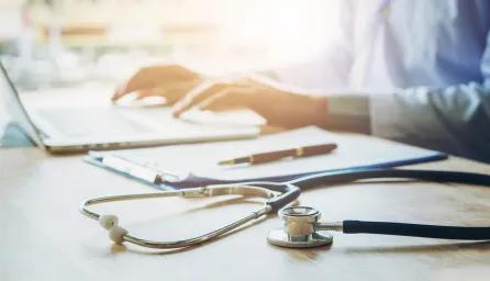 Person working at laptop with stethoscope on desk next to them