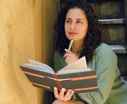 Lady holding a book with a pen in hand, thinking