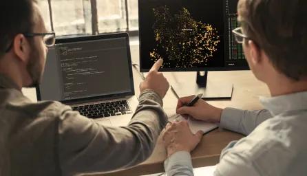 Two people discussing data at 2 computers 