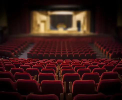 Looking down at a stage in an empty theatre of red seats