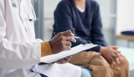 Person in white coat with stethoscope and notes talking to someone