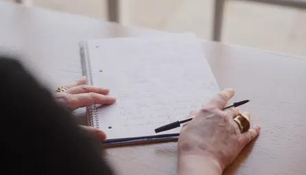 Close up of a woman's hands, poised ready to continue writing on paper