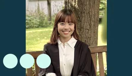 Asian woman sat on bench in graduation gown