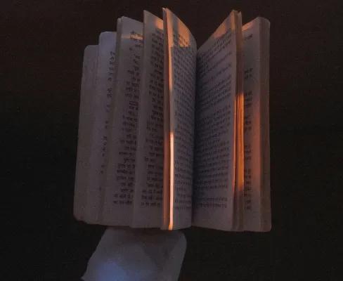 A gloved hand holding a book, with the book partially open and set against a black background