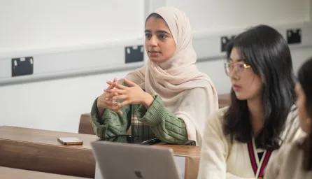 Young women sitting at desk listening to professor