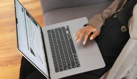 A person sitting on a sofa with an open laptop in their lap.