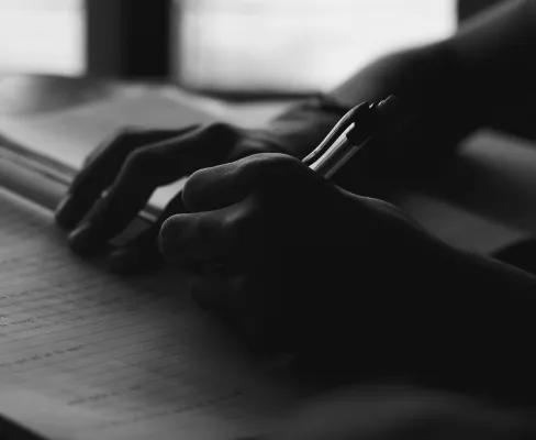 A person writing in a notepad filled with handwriting, shown in black and white