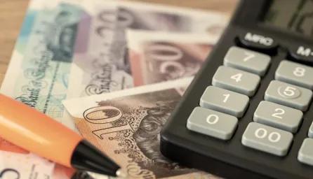 A calculator resting on British banknotes with a pen beside them on a table