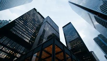 A low-angle view of several lit-up skyscrapers against a cloudy evening sky.