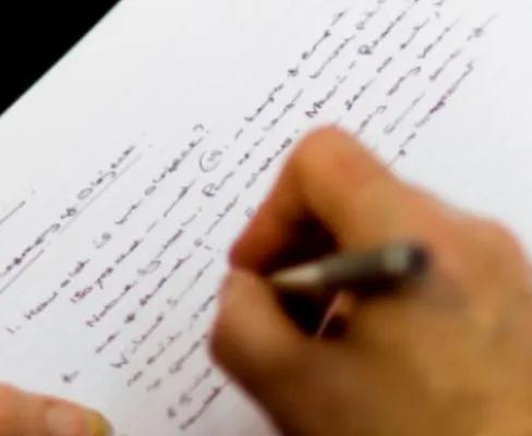 A hand holding a pen, writing in a lined notebook.