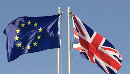 The European Union flag and the Union Jack (UK flag) flying side-by-side against a blue sky.