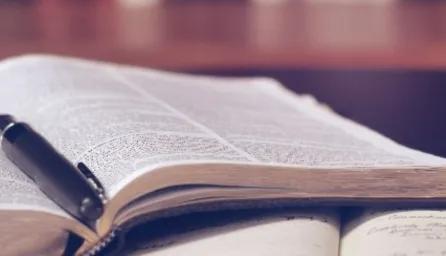 Open philosophical book with a pen resting in the center, pages slightly curved, and a softly blurred background.