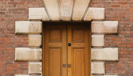 Double wooden doors set within a decorative surround of large sandstone blocks and a brick wall.