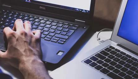 Close-up of a person's hands as they're working at a black laptop, another open silver laptop next to it.