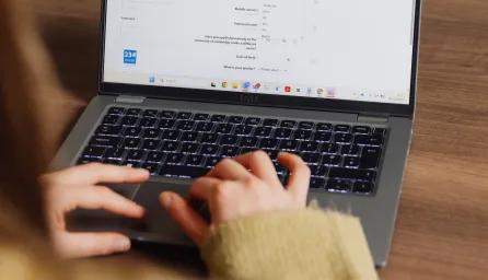 Close-up of a woman's hands and laptop screen as she types, taken from an over-the-shoulder perspective.