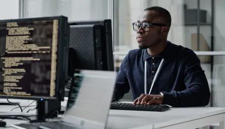 Young developer in eyeglasses concentrating on his online work on computer sitting at workplace