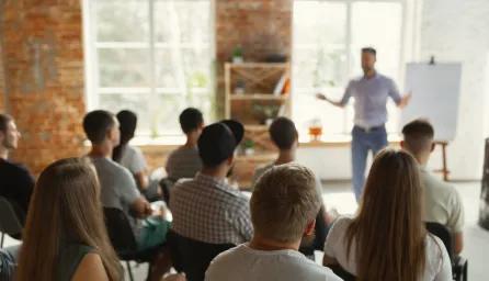 Male speaker giving presentation in hall at university workshop. Audience or conference hall. Rear view of unrecognized participants in audience. Scientific conference event, training. Education concept.