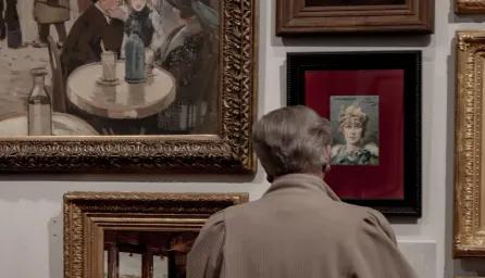 A man standing, looking at some paintings on a wall