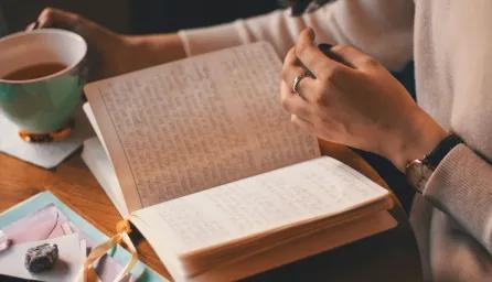 Photo of a person reading a book and holding a cup of tea