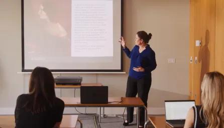 A woman stands and presents at the front of a classroom.