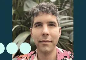 Man with greying dark curly hair, stood in front of large plant 