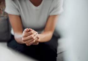 A person with clasped hands leaning forward on a couch