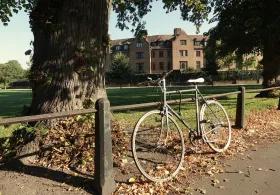 Bicycle leaning against railings by a lawn in front of a college