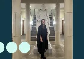 Woman in graduation gown stood in front of a statue 