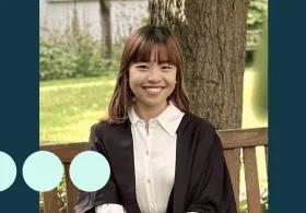 Asian woman sat on bench in graduation gown