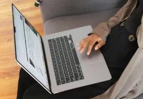 A person sitting on a sofa with an open laptop in their lap.