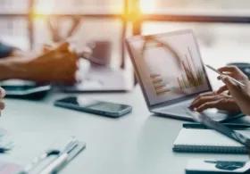 Cropped shot of people sitting on either side of a table, only their arms and hands visible, and an open laptop.