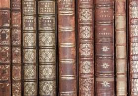 A collection of old, leather-bound books with gold accents on wooden library shelves.