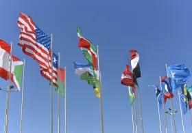 Multiple national flags from various countries, wave in the wind against a clear blue sky.