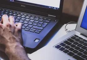 Close-up of a person's hands as they're working at a black laptop, another open silver laptop next to it.