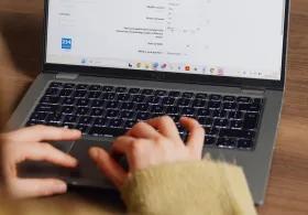 Close-up of a woman's hands and laptop screen as she types, taken from an over-the-shoulder perspective.