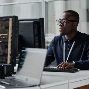 Young developer in eyeglasses concentrating on his online work on computer sitting at workplace