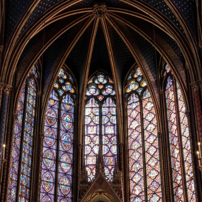 Multicoloured tall stained glass windows viewed from the inside of Sainte Chapelle looking up towards the ceiling.