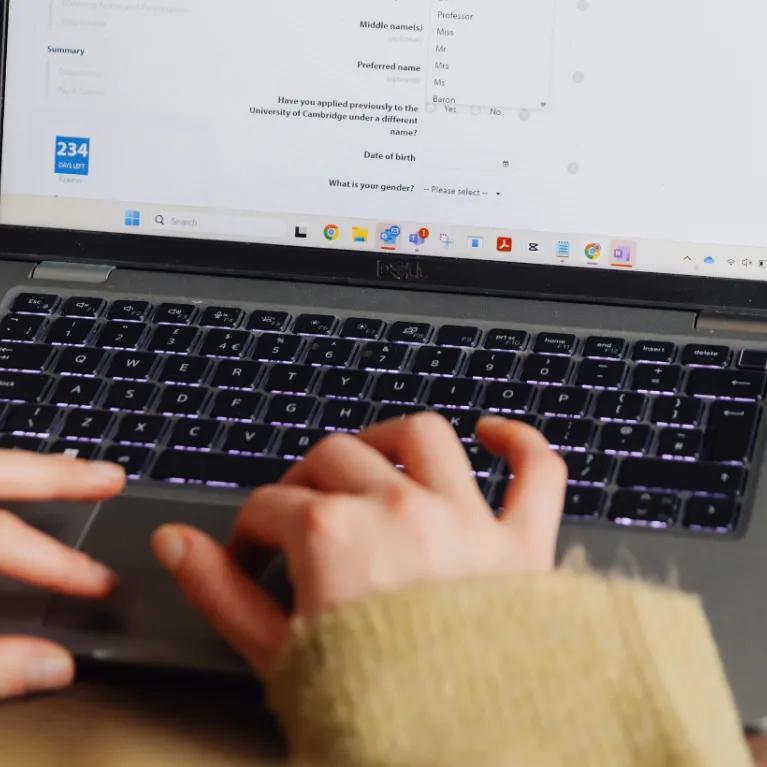 Close-up of a woman's hands and laptop screen as she types, taken from an over-the-shoulder perspective.