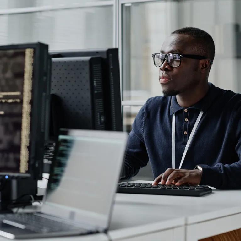 Young developer in eyeglasses concentrating on his online work on computer sitting at workplace
